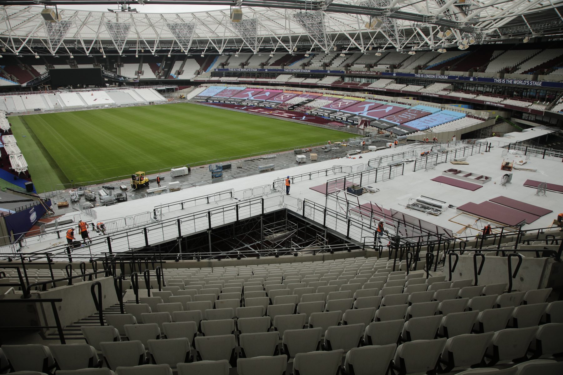 Looking down from the upper seating at the London Stadium in 2020, as crews in hi-vis build a raised deck over the lower seating beside the pitch
