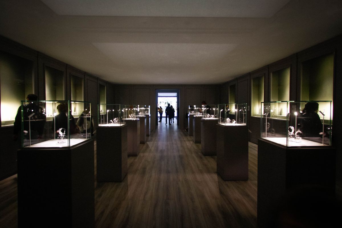 A long, dimly lit gallery of illuminated watch vitrines at the Patek Philippe exhibition, Saatchi Gallery